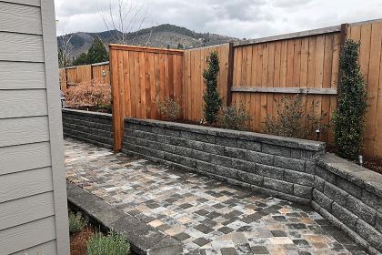 stone retaining wall design incorporates fencing and garden beds